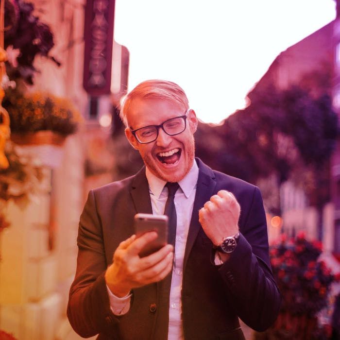 Um homem profissional do mercado imobiliário comemorando com o smartphone em mãos.
